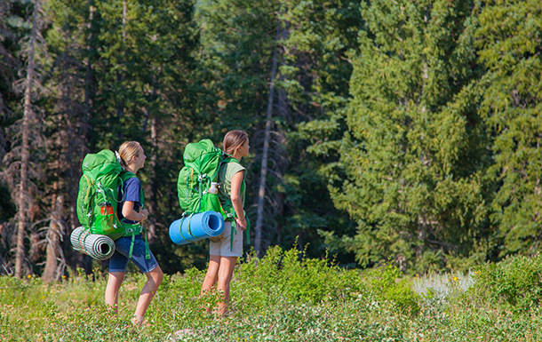 Two Girl Scouts standing outside wearing camping equiped backpacks 