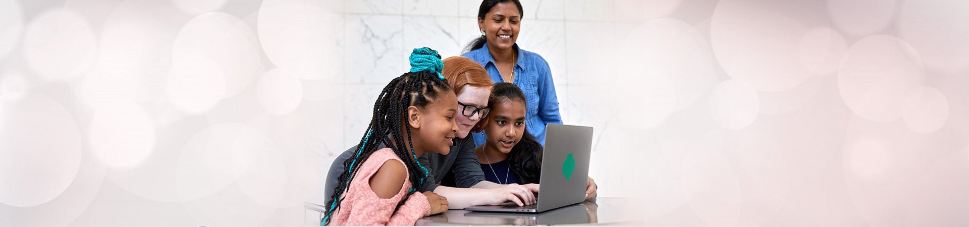  Three elementary school Girl Scouts sitting at laptop computer with adult volunteer watching over them. 