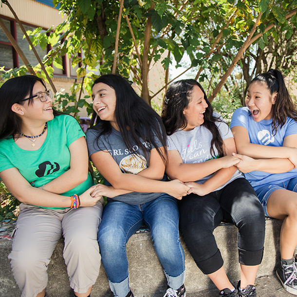 group of high school girl scouts holding hands outside in a seated friendship circle smiling and laughing