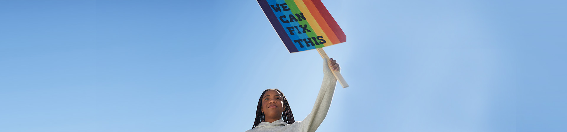  High school senior ambassador Girl Scout holding sign that reads "We can fix this" with rainbow stripes. 