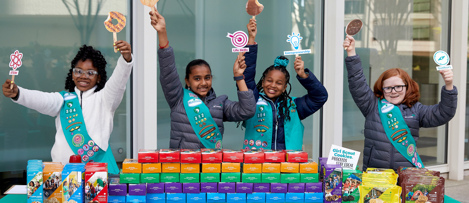  Junior Girl Scout Troop holding up signs at a cookie booth 