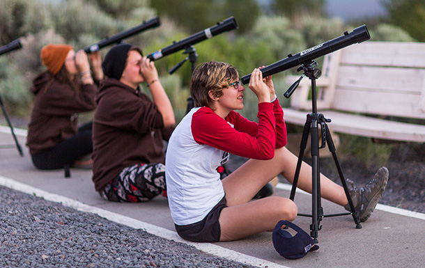 Three older Girl Scouts sitting and looking through telescopes